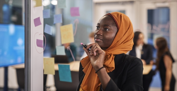 Image of a Thunderbird student writing on a board with post it notes during a meeting